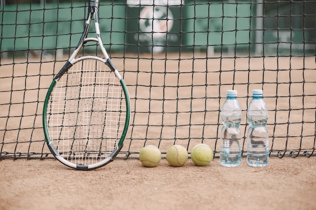 Игроки оставили теннисные мячи, ракетку и две бутылки воды на теннисном корте
