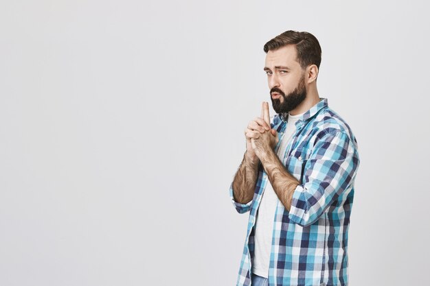 Playful adult bearded man acting like secret agent, blowing at finger gun