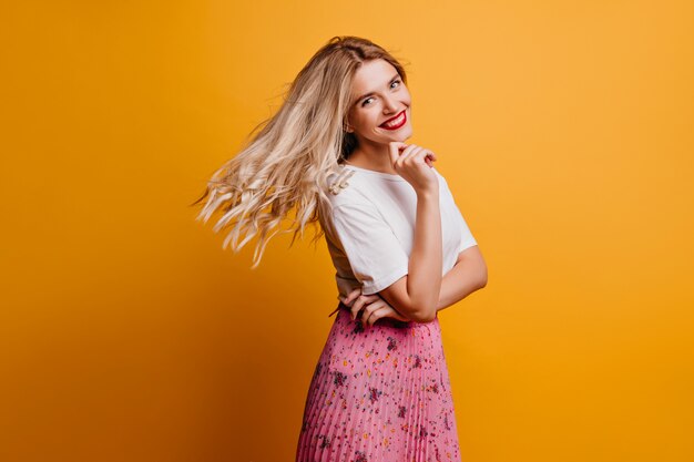 Игривая блондинка, выражающая счастье. изысканная стильная дама на оранжевой стене.