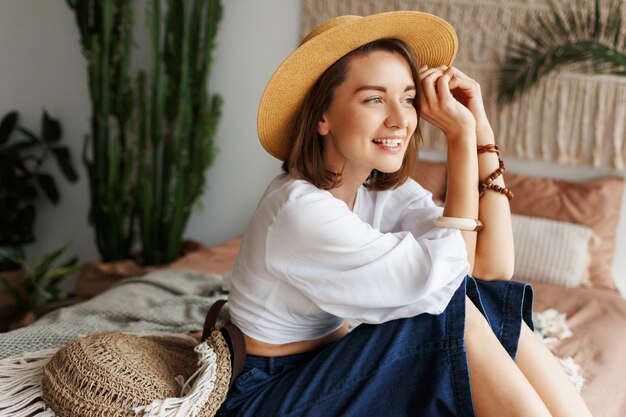 Playful bohemian woman posing in stylish bedroom with amazing interior