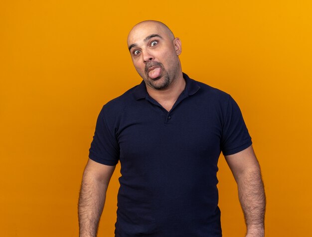 Playful casual middle-aged man  showing tongue isolated on orange wall