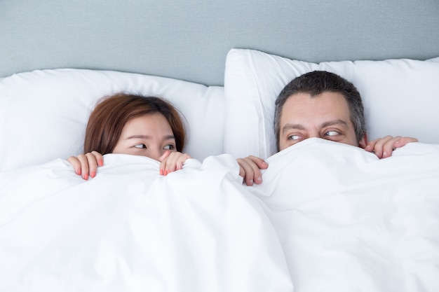 Playful couple hiding behind blanket in bed
