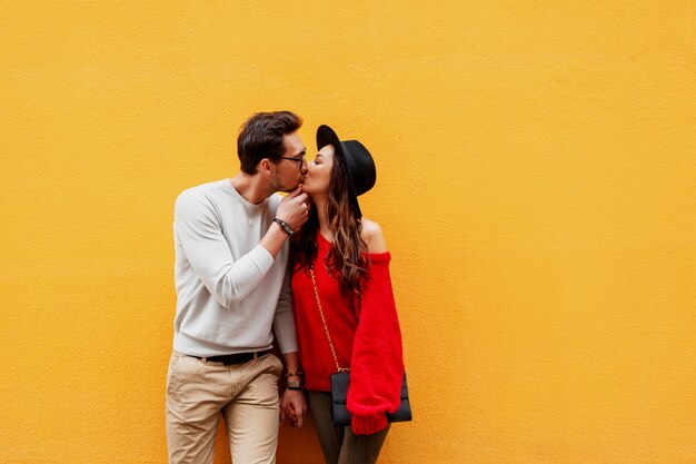 Playful couple in love posing over yellow wall. Traveling people. Brunette girl with handsome boyfriend traveling in Europe.