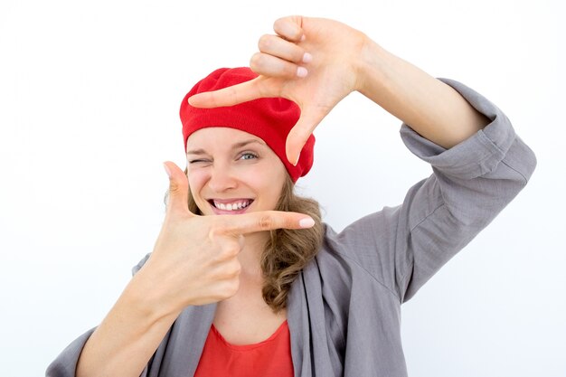 Playful creative businesswoman focusing on project. Cheerful young French woman looking through hands and winking. Business approach concept