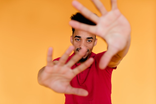 Free photo playful exited charming man covering face with hands over yellow wall.