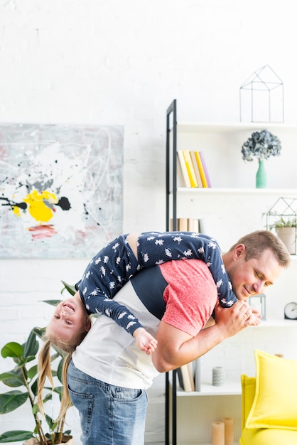 Free photo playful father carrying her happy daughter in living room