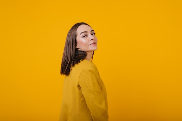 Free photo playful girl looking over shoulder while posing. spectacular female model in bright jacket enjoying.