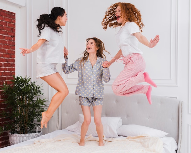 Playful girlfriends jumping in bed