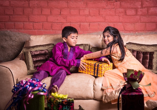 소파에 앉아있는 동안 웃거나 선물을 위해 싸우는 디 왈리 선물로 민족 착용에 쾌활한 인도 아시아 어린이