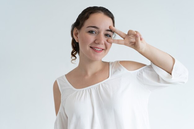 Playful lovely woman showing victory sign and looking at camera