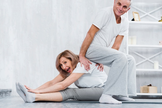 Playful man sitting on back of his wife while doing yoga at home