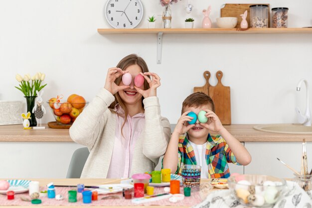 Playful mom and son covering eyes with painted eggs