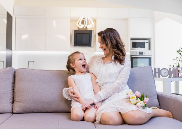 Playful mother and daughter looking at each other sitting on sofa