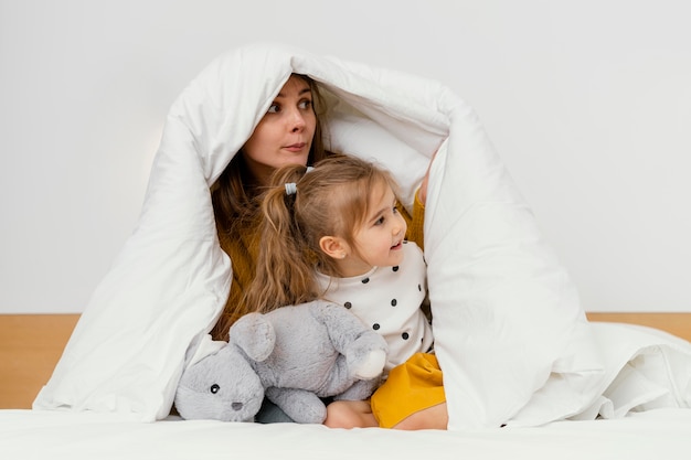 Playful mother and kid hiding under blanket