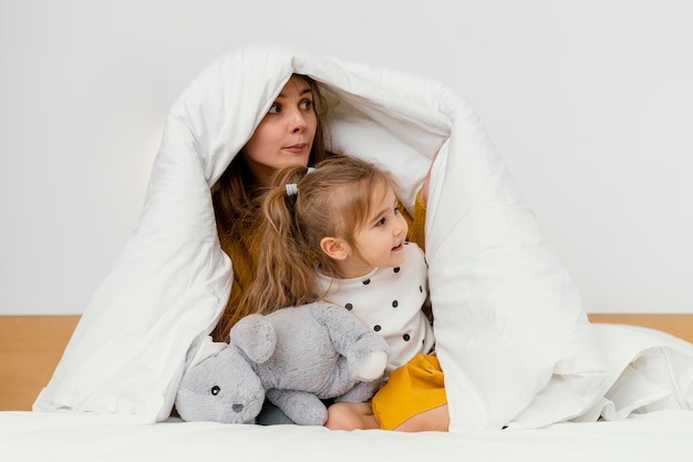 Игривая мать и ребенок прячутся под одеялом