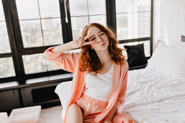 Playful red-haired lady spending weekend morning in her flat. Positive appealing woman posing in pajama.