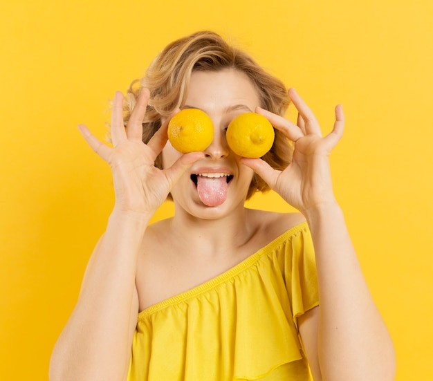 Playful woman covering eyes with lemons