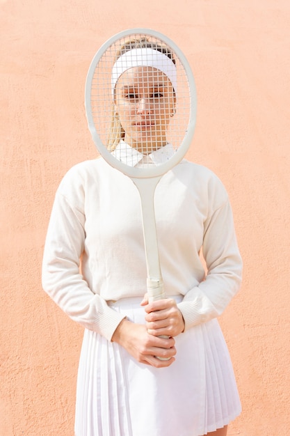 Foto gratuita donna allegra che copre il viso con la racchetta da tennis