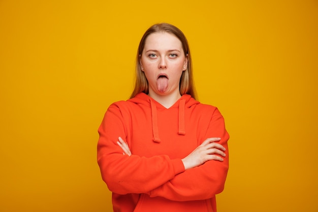 Playful young blonde woman standing with closed posture showing tongue 