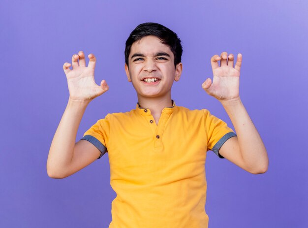 Игривый молодой кавказский мальчик делает тигровый рык и жест лап, изолированные на фиолетовой стене