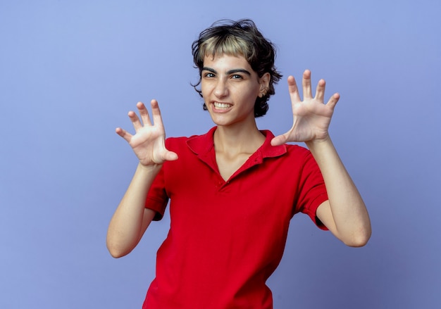 Playful young caucasian girl with pixie haircut doing tiger paws gesture isolated on purple background with copy space