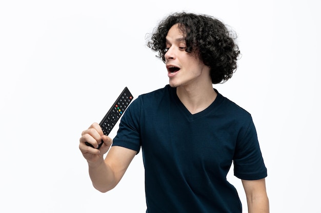 Free photo playful young handsome man using remote control as microphone looking at it singing isolated on white background