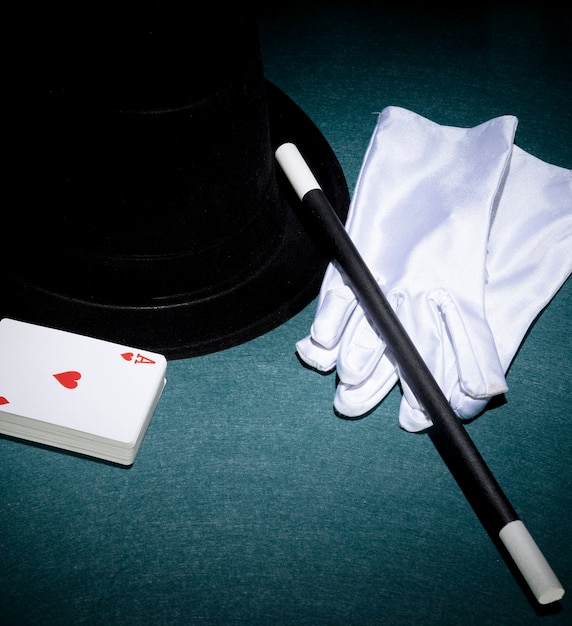 Free photo playing cards; white gloves; top hat and magic wand on green background