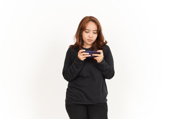 白で隔離の黒いシャツを着ている美しいアジアの女性のスマートフォンでモバイルゲームをプレイ