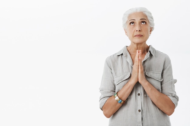 Умоляющая старшая дама смотрит вверх, взявшись за руки в молитве, молясь