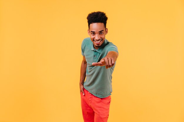 Pleasant african man pointing finger. Indoor shot of interested black boy posing.