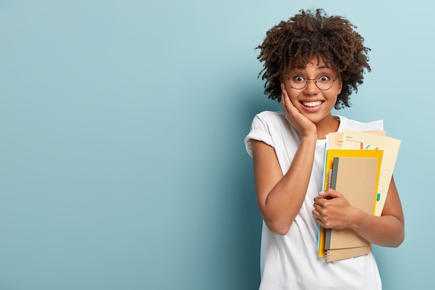 Pleasant looking Afro American woman holds notepads, papers, studies at college, glad to finish studying
