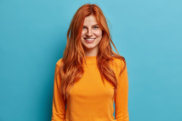 Pleasant looking ginger woman with freckles smiles broadly dressed in long sleeved jumper has happy mood.