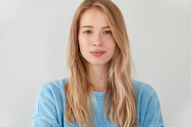 Pleasant looking serious blonde woman with long hair, wears blue casual sweater