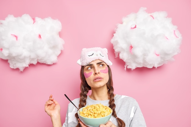 Pleasant looking thoughtful woman concentrated above wears sleepmask and pajama