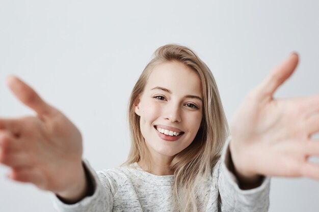 抱擁のために腕を伸ばして広い笑顔で快適そうに見える若い白人女性