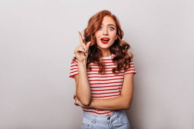 Pleasant white girl in casual attire posing with surprised smile. Appealing curly woman expressing amazement.