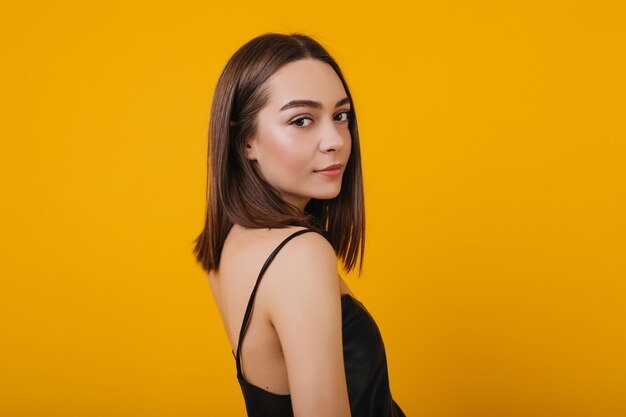 Pleasant young lady looking over shoulder while posing. Portrait of lovely  girl in black tank-top chilling