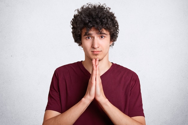 Free photo please, forgive me! handsome young curly male makes praying gesture