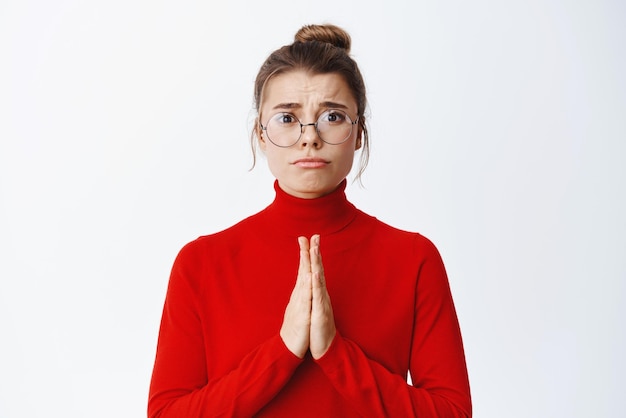 Free photo please help me miserable young woman clinging holding hands in pray pleading or begging for something standing in glasses against white background