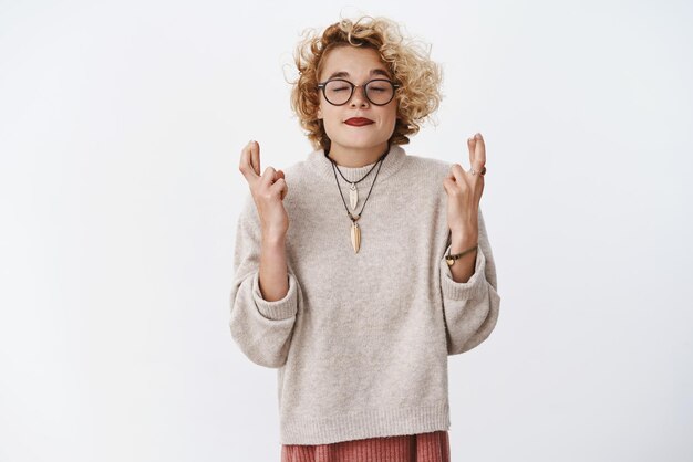 Please I wanna this gift Portrait of hopeful cute girl believer close eyes and faithfully cross fingers for good luck as making wish and praying for dream come true posing over white background