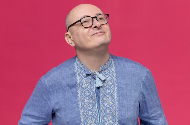 Pleased adult slavic man in blue shirt wearing optical glasses looking up 