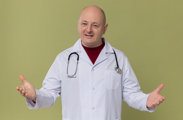 Pleased adult slavic man in doctor uniform with stethoscope keeping hands open and 