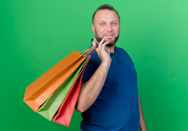 Foto gratuita uomo slavo adulto soddisfatto che tiene i sacchetti della spesa sulla spalla isolata sulla parete verde con lo spazio della copia