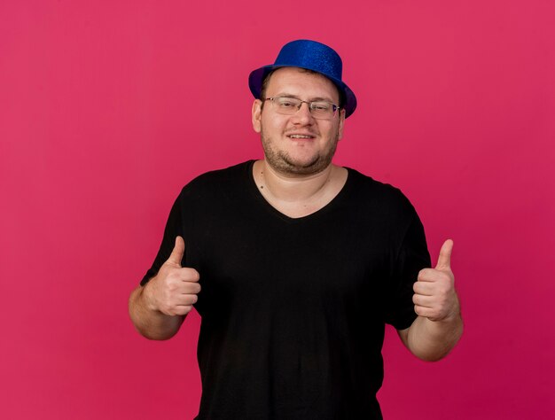 Pleased adult slavic man in optical glasses wearing blue party hat thumbs up with two hands 