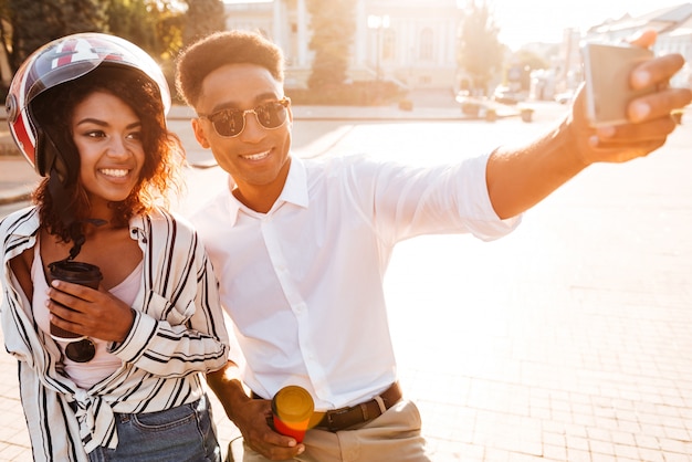 Pleased african couple making selfie on smartphone while being on the street