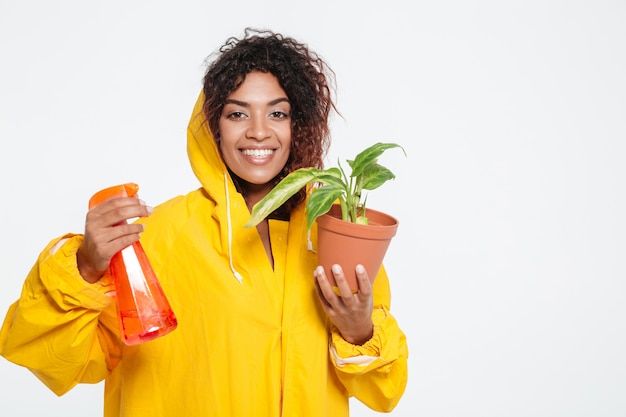 Pleased african woman in raincoat holding plant