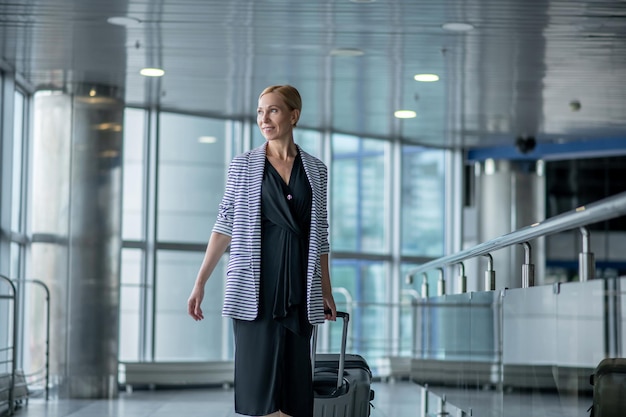 Pleased airport passenger with her baggage looking away