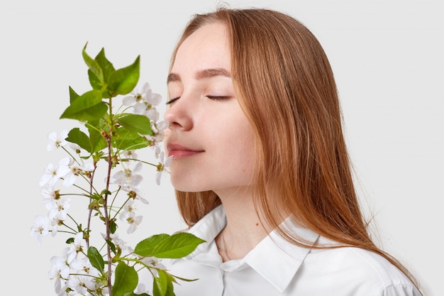 Pleased attractive woman smells cherry blossom