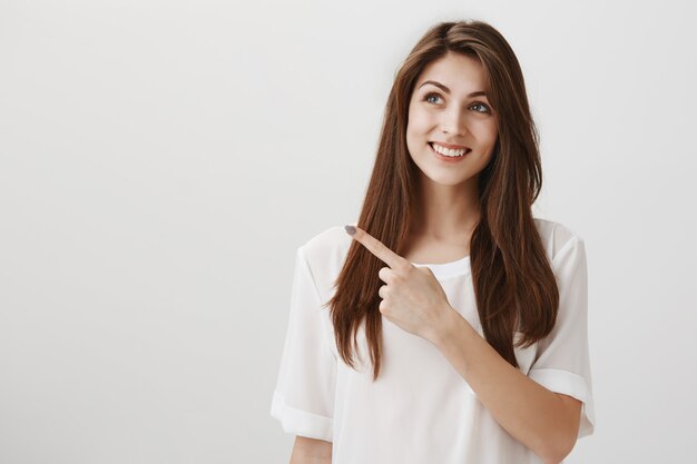 Pleased beautiful woman pointing and looking upper left corner with happy smile