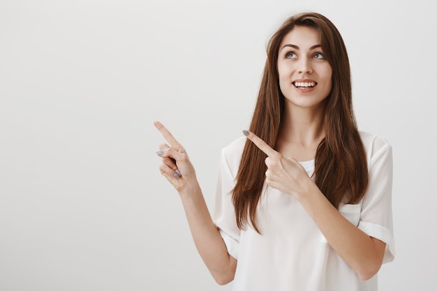 Felice bella donna che punta e guarda nell'angolo in alto a sinistra con un sorriso felice